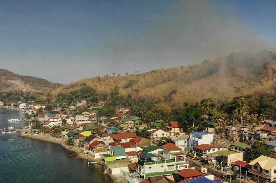 Thick smoke envelopes Barangay San Jose in Mabini, Batangas as fire rages on the mountainside in Pulong Anahao or Barangay Santa Ana on April 21, 2024.