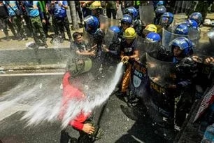 A demonstrator blocks personnel from the Bureau of Fire Protection and the Philippine National Police as they attempt to extinguish the burning 'Trio Delubyo' effigy during a Labor Day protest in Manila on Friday, May 1, 2026. The move to extinguish the fire comes as national law bans open burning, particularly in public spaces. Maria Tan, ABS-CBN News