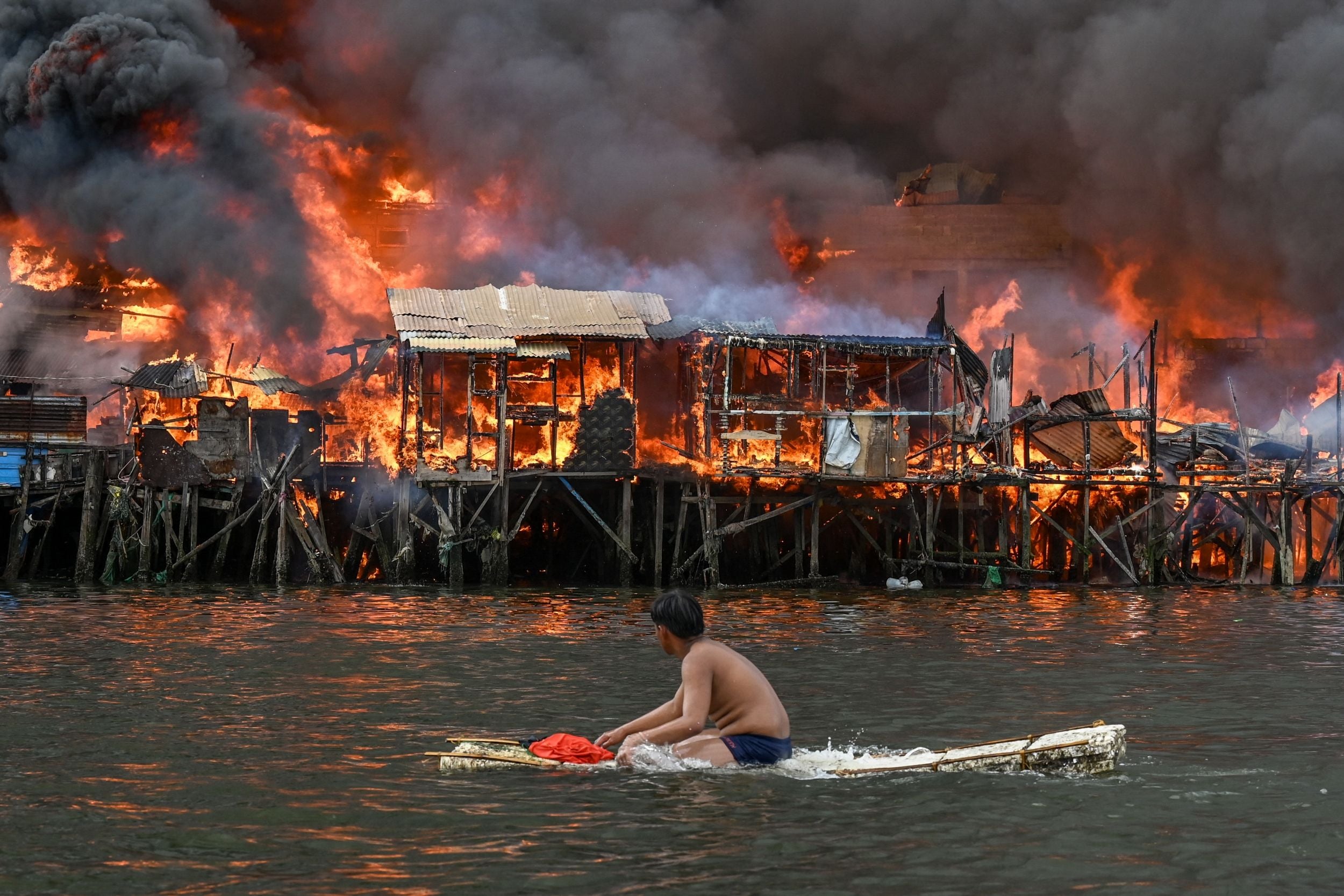 A man watches houses on fire at Tondo in Manila on Sunday. Raging orange flames and thick black smoke billowed into the sky, as fire ripped through hundreds of houses in a closely built slum area of the Philippine capital Manila. Jam Sta. Rosa, AFP
