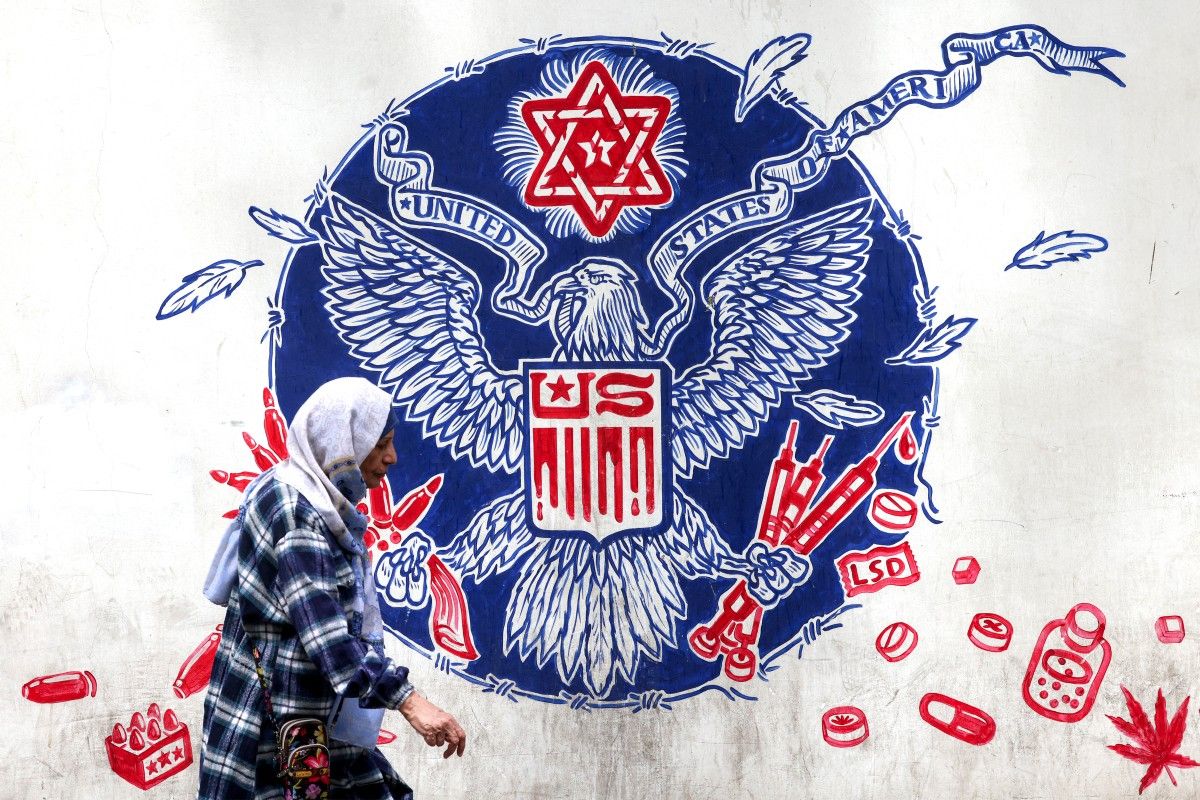 A woman walks past a mural depicting a mock version of the Great Seal of the United States, with the eagle holding syringes and ammunition cartridges in its talons and a Star of David painted above with other drugs and firearms nearby, painted on the outer walls of the former US embassy in Tehran, colloquially-referred to as the "Spy Den," on April 8, 2025. Atta Kenare, AFP/File